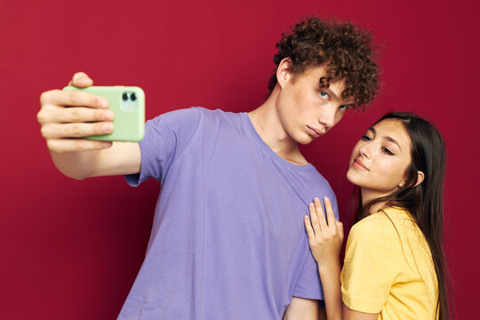 young man and girl in colorful T-shirts with a phone red background