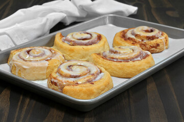 Freshly baked cinnamon rolls on a baking sheet.  Selective focus on front roll.