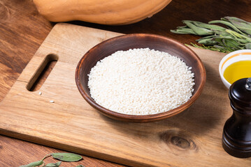 Ingredients for making risotto with pumpkin on the kitchen table - rice in a bowl, pumpkin, olive oil, herbs