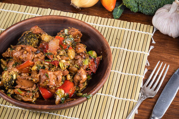 Stewed chicken with vegetables in a plate on the table with ingredients for cooking around, close-up