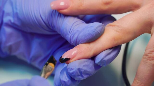 close-up of a manicurist paints a black French on the client's nails with a brush.