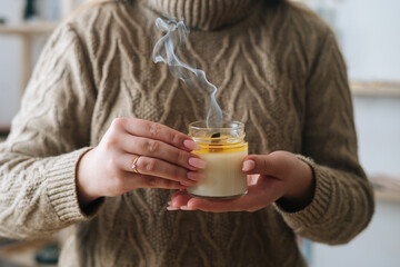 Close-up cropped shot of unrecognizable young woman holding extinguished handmade candle in glass...