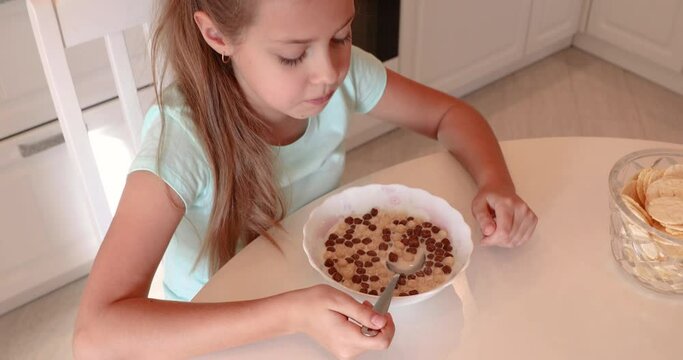 Breakfast in the kitchen. the baby has breakfast. the girl eats flakes with milk. useful children's breakfast