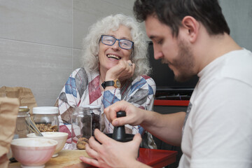 Mature mother laughing while is in the kitchen with her adult son.