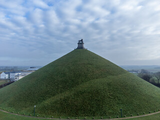  Lion's Mound from a distance and dramatic clouds. Butte Du Lion on the battlefield of Waterloo where Napoleon was defeated. Drone aerial view.