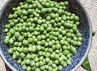 Raw shelled peas in an oriental bowl with blue designs.