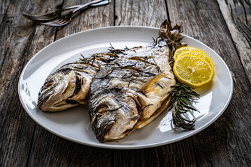 Roast sea bream with rosemary and lemon on wooden table
