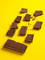 Broken milk chocolate bar. On yellow isolate.