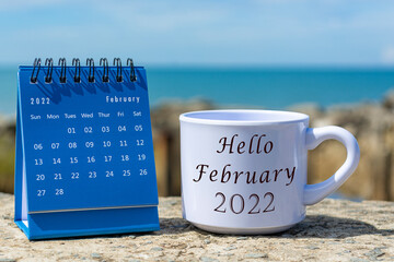 Hello February 2022 written on white coffee cup with blue calendar