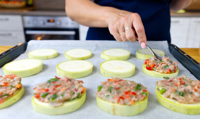 Obraz na płótnie Canvas Zucchini stuffed with raw minced meat and vegetables on a baking sheet. female hands spread the minced meat on zucchini circles. The process of making dinner. close up