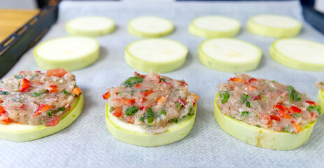 Zucchini stuffed with raw minced meat and vegetables on a baking sheet. female hands spread the minced meat on zucchini circles. The process of making dinner. close up