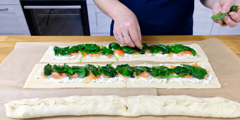 the cook puts spinach and trout on the dough. Savory Christmas pie in the shape of a wreath cooking process. close up