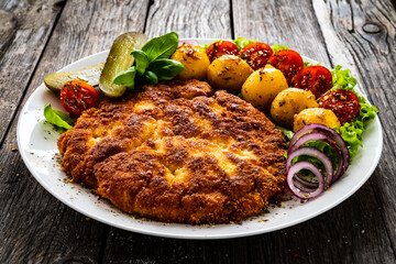 Breaded fried pork chop with fried potatoes and vegetables on wooden table
