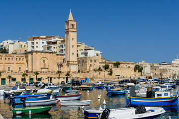 Fototapeta na wymiar Boats on Marsaskala Harbour with the Parish Church in the background, Marsaskala, Malta.