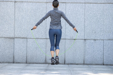 Fitness woman rope skipping against city wall
