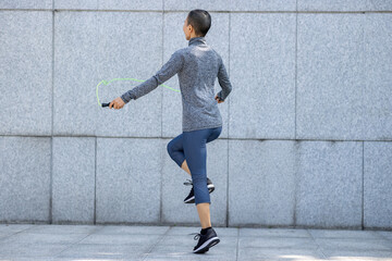 Fototapeta na wymiar Fitness woman rope skipping against city wall