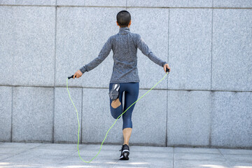 Fitness woman rope skipping against city wall