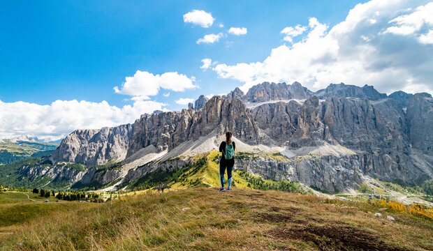 Aerial view of female sport hiker looking at Gardena Pass, Sass da Ciampac, Piz Boe, Tor Bornech and Sass dla Luesa, Trentino Alto Adige, Italy. Alpine meadows and Passo Gardena.