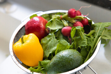 Close up shoot of sweet yellow pepper, green arugula, radish in strainer on the white kitchen sink