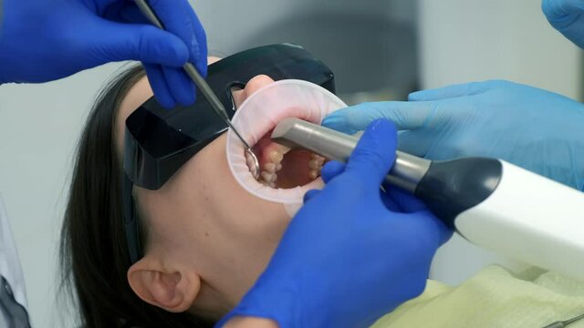 Dentist is doing intraoral scanning for woman before installing ceramic veneers and crowns. Orthodontist holds in his hand a manual 3D scanner for the jaw and mouth. Prosthodontics concept.