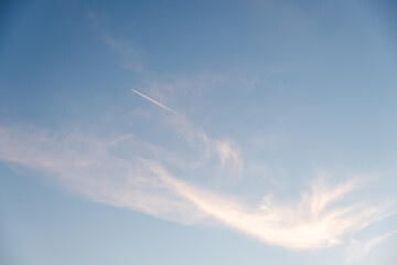 Naklejka na ściany i meble Airplane contrasting with sky at sunset. Airplane tracks over blue sky