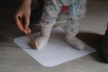 Checking baby foot size mother holding leg of her child on the blank paper drawing around with...