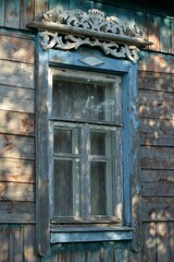 Old wooden window. Blue trim. Board wall. Spots of light on the wall of a village house. White wooden carved home decoration. Handmade. Ancient building. Old village house. 