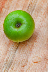 fresh and crisp green granny smith apples on wooden surface with water droplets