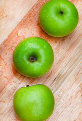 fresh and crisp green granny smith apples on wooden surface with water droplets