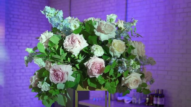 Flower arrangement at the party. Decorated with pink and white rose flowers and greenery at a wedding reception. Stage light on the background, indoors.