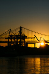 Silhouette of cranes at the Port of Lisbon, Portugal with 25 April Bridge in background