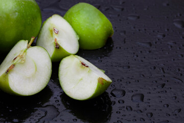 fresh and crisp green granny smith apples on black surface with water droplets