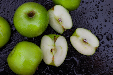 fresh and crisp green granny smith apples on black surface with water droplets