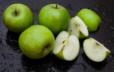 fresh and crisp green granny smith apples on black surface with water droplets