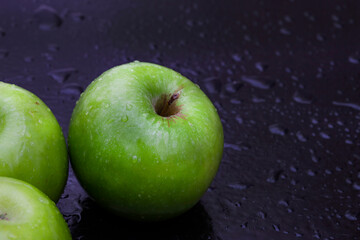 fresh and crisp green granny smith apples on black surface with water droplets