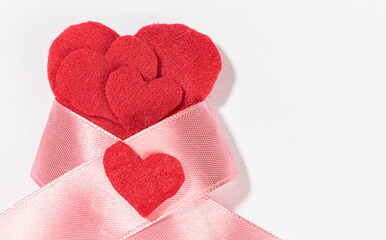 Fototapeta premium A lot of red felt hearts with a pink ribbon bow isolated on a white background on the left