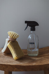 Glass spray bottle anti-calc product and natural wash sponge and brush on wooden surface on white wall background. Home made cleaning detergent recipe. Eco friendly zero waste household concept.