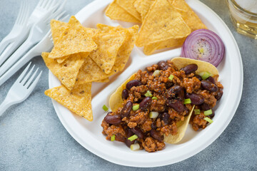 Nachos chips with minced meat and beans served on a white takeaway plate, close-up, horizontal shot