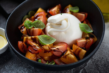 Salad with burrata cheese, tomatoes, balsamic and fresh green basil served in a black bowl, close-up