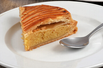 Portion de Galette des rois à la frangipane servie dans une assiette avec une cuillère en gros plan