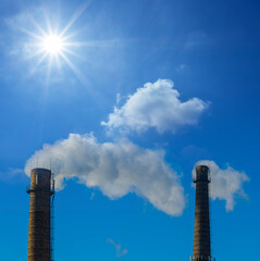 closeup pair of industrial pipes with smoke on blue sunny sky background, concept ecological scene