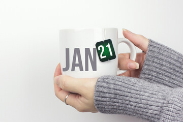 January 21st . Day 21 of month, Calendar date. Closeup of female hands in grey sweater holding cup of tea with month and calendar date on teabag label. Winter month, day of the year concept.