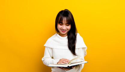 Fototapeta premium photo of asian girl smiling while reading a book while smiling on a yellow background book reading concept a little girl who loves to read books