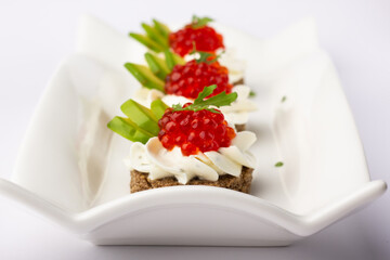 Smorrebrod. A delectable ensemble of red caviar canapés, accentuated with fresh avocado and cream, artistically placed on a uniquely shaped white dish for a modern touch.