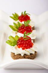 Smorrebrod. Gastronomic artistry showcased in these rye-based appetizers, crowned with lustrous red caviar and cream, complemented by green avocado, all poised for indulgence.