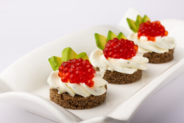 Smorrebrod. Gourmet appetizers featuring luscious red caviar atop creamy spread, set on rye bread with fresh avocado slices, elegantly served on a modern white dish.
