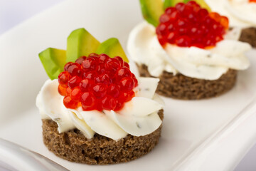 Close-up of luxurious canapés, crowned with glistening red caviar, paired with a velvety cream base, all presented on a rye canvas, highlighting culinary finesse. Smorrebrod. Canapes with red caviar