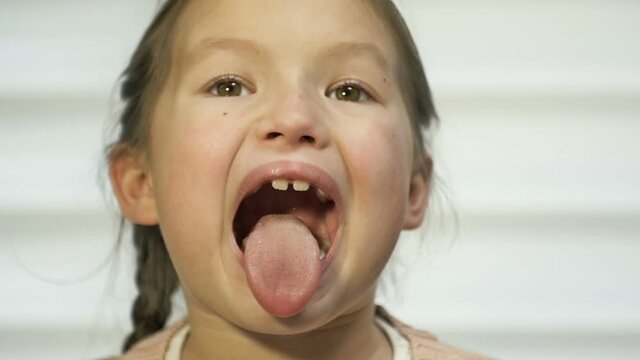 Girl of 7-8 years old diligently shows her tongue. Perhaps at a doctor's appointment.