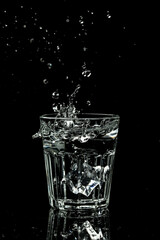 Close up view of the ice cubes splash in water are isolated on a black background. vertical image, place for text