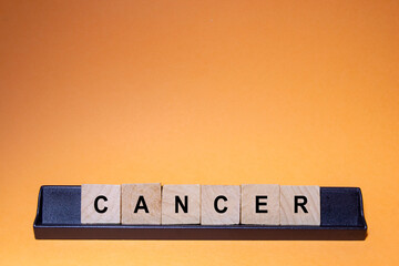 CANCER. Word written on square wooden tiles with an orange background. Horizontal photography.